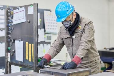 粉塵マスクとヘルメット、作業着を着用しデスクの上で作業を行う男性