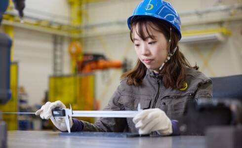 ヘルメットをかぶった女性が機械の作業をしている様子を示す画像