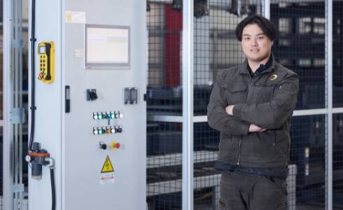 作業着姿の男性が機械の前でポーズをとっている様子