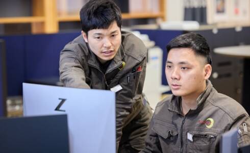 二人の作業着を着た男性が制服を着て、コンピュータの画面を見つめている様子