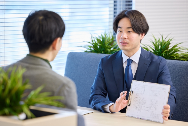スーツ姿の男性がボードを手に説明する様子