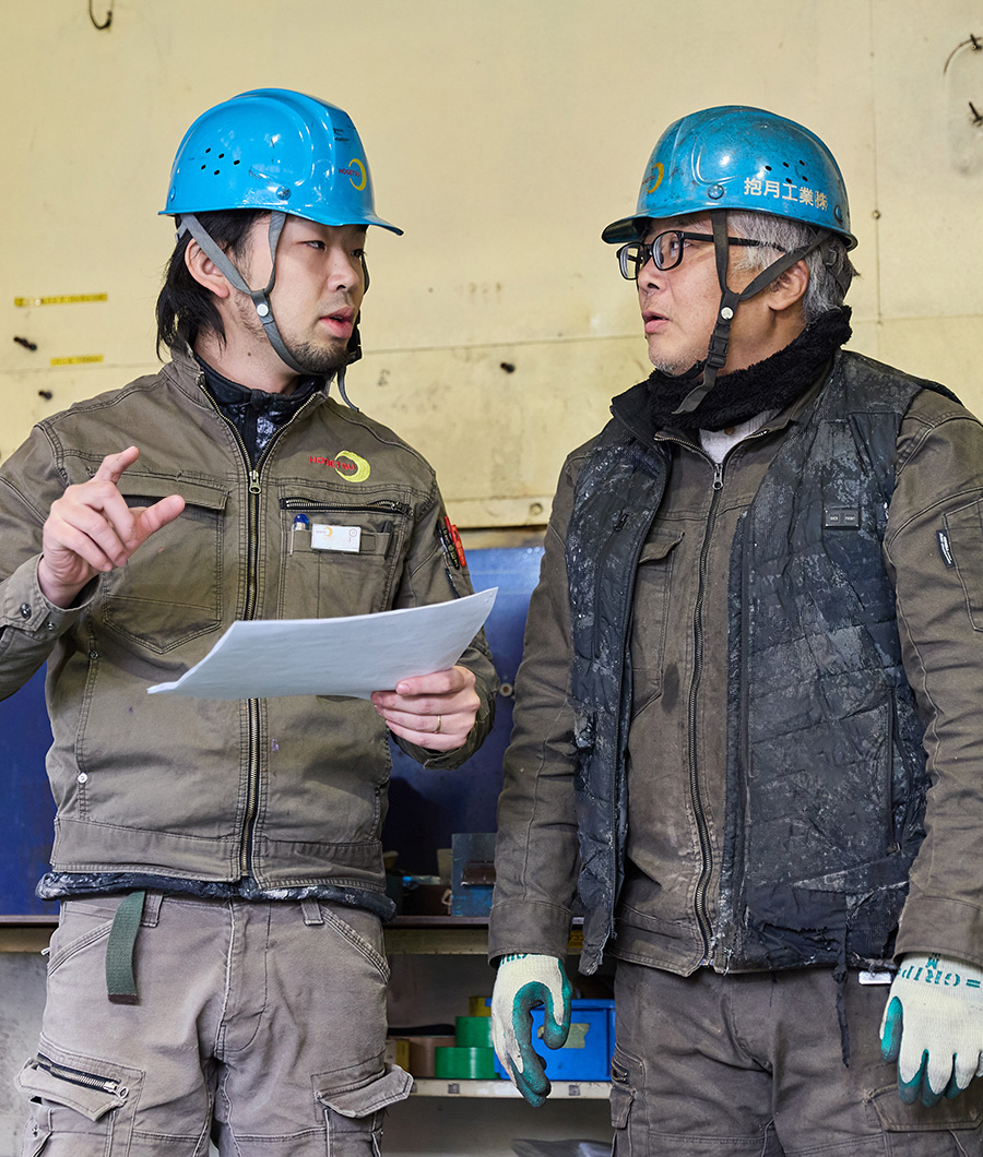 ヘルメットと作業着を着て工場内で作業をする女性。