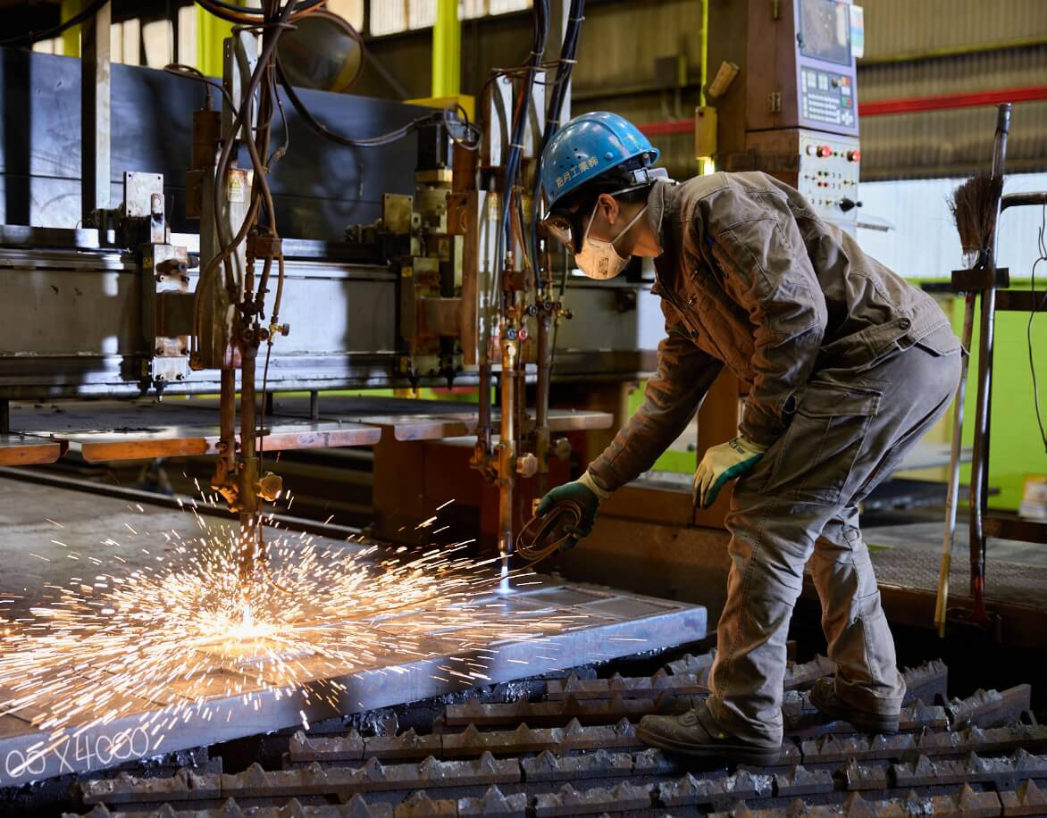 工場内で鉄板を加工する様子。機械からは火花が散っている