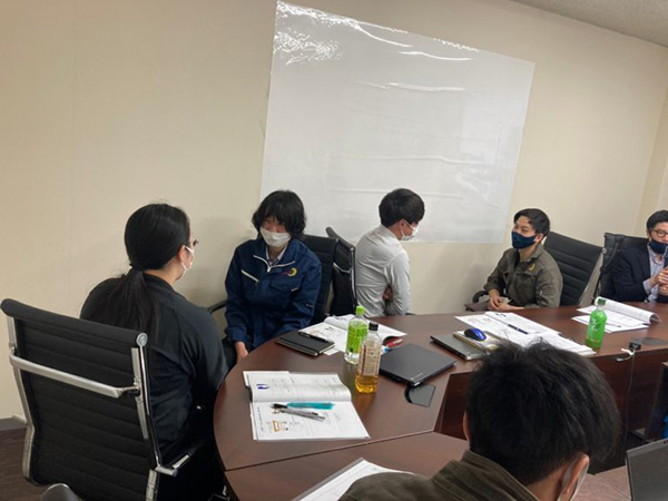 テーブルの周りに集まった人々が、資料を見ながら議論している場面。