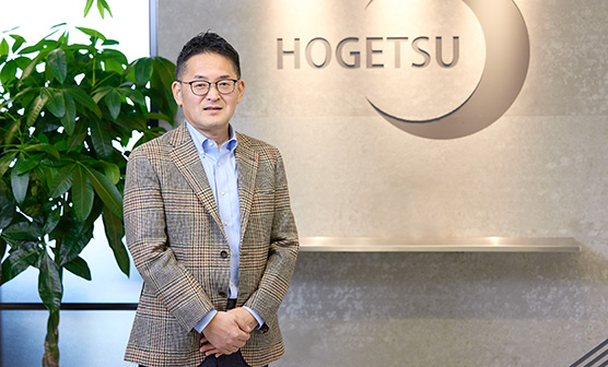 抱月工業株式会社のエントランス前で会社ロゴを背景に写る社長