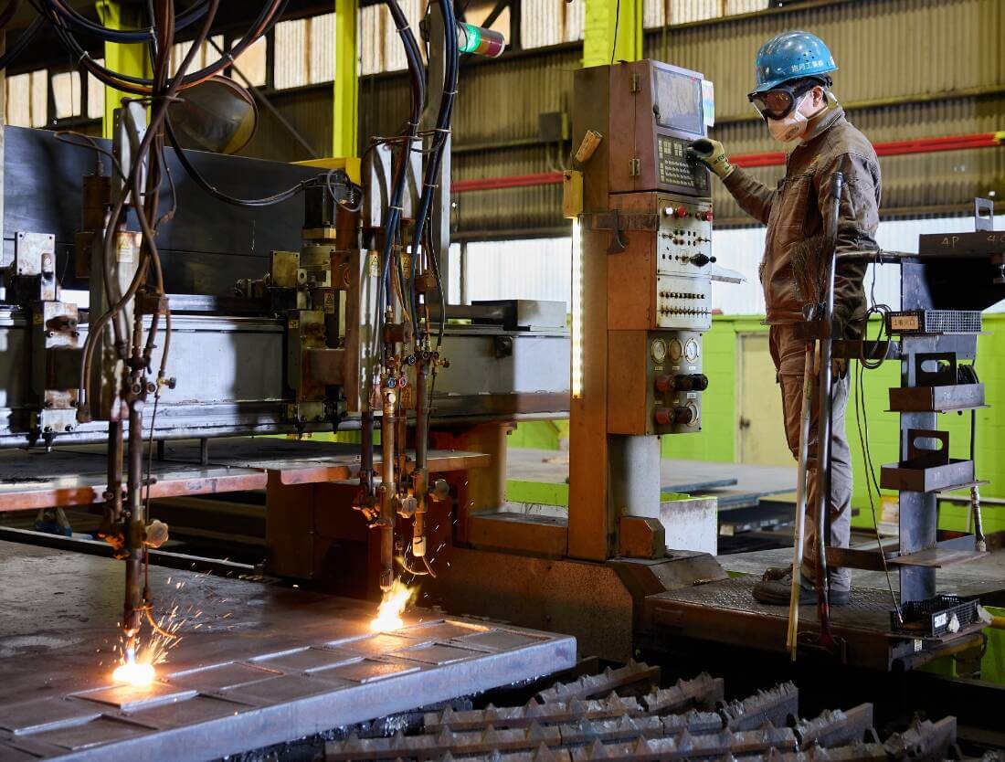 工場内で機械を操作する男性。操作している機械からは火花が散っている。