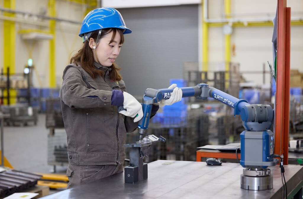 ヘルメットと作業着を着て工場内で作業をする女性。